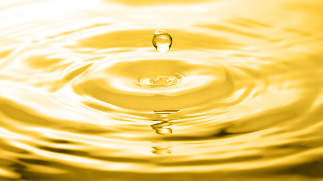 Makroaufnahme eines Tropfens, der konzentrische Wellen auf einer gelben Flüssigkeit erzeugt