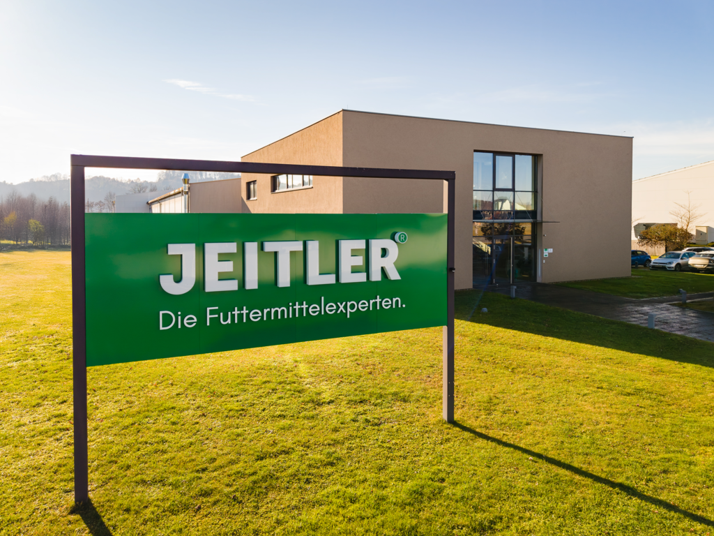 Grünes Firmenschild mit dem Schriftzug "JEITLER" und dem Slogan "Die Futtermittelexperten" vor einem Firmengebäude