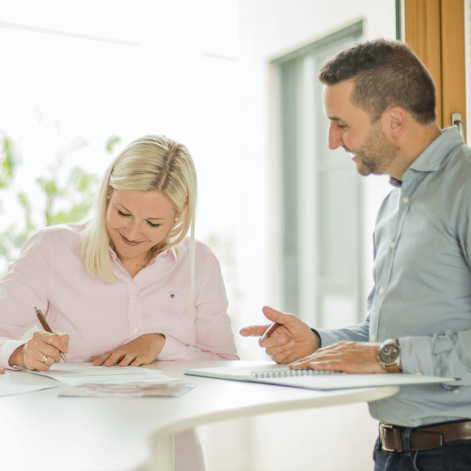 Ein Mann und eine Frau besprechen Dokumente an einem Tisch, während die Frau Notizen macht