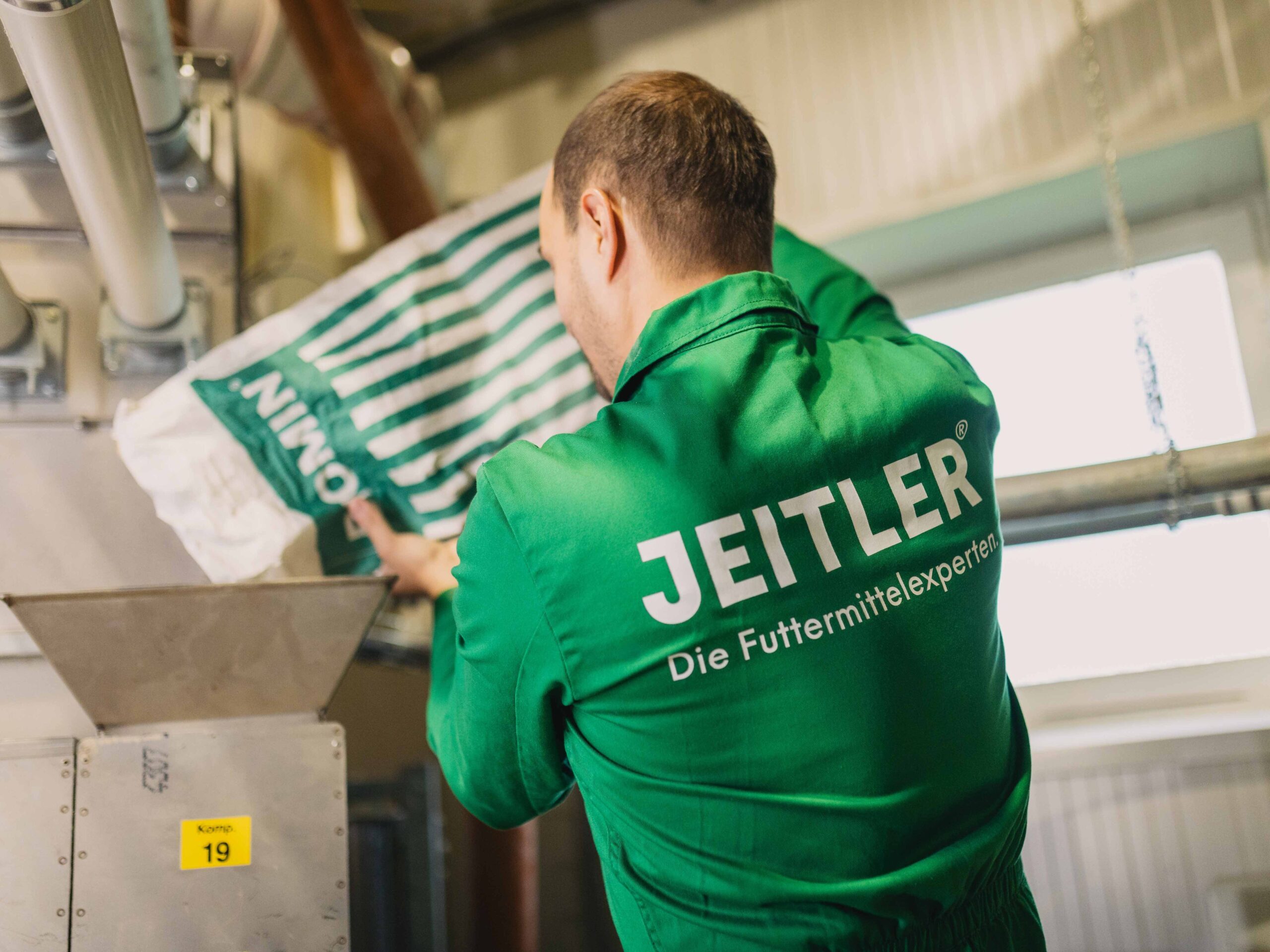 Ein Mitarbeiter in grüner Arbeitskleidung leert einen Futtersack in eine Maschine