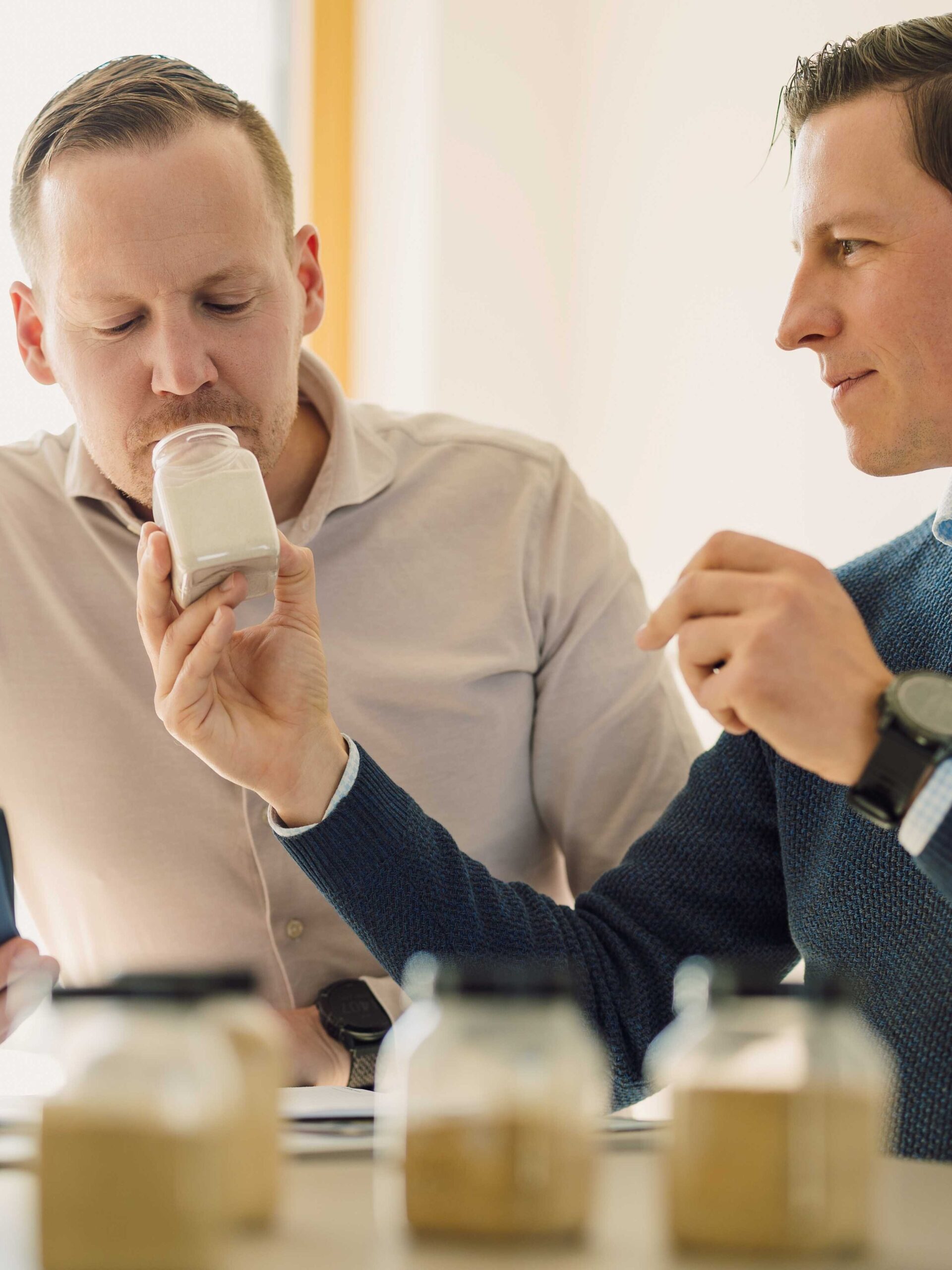 Zwei Männer testen den Geruch eines Produktes aus einem Glasbehälter