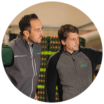 Zwei Mitarbeiter in grauen Arbeitsjacken schauen zur Seite